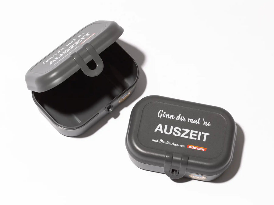 Zwei graue Brotdosen mit BÜRGER-Logo und Spruch „Gönn dir mal ’ne Auszeit“ auf weißem Hintergrund.