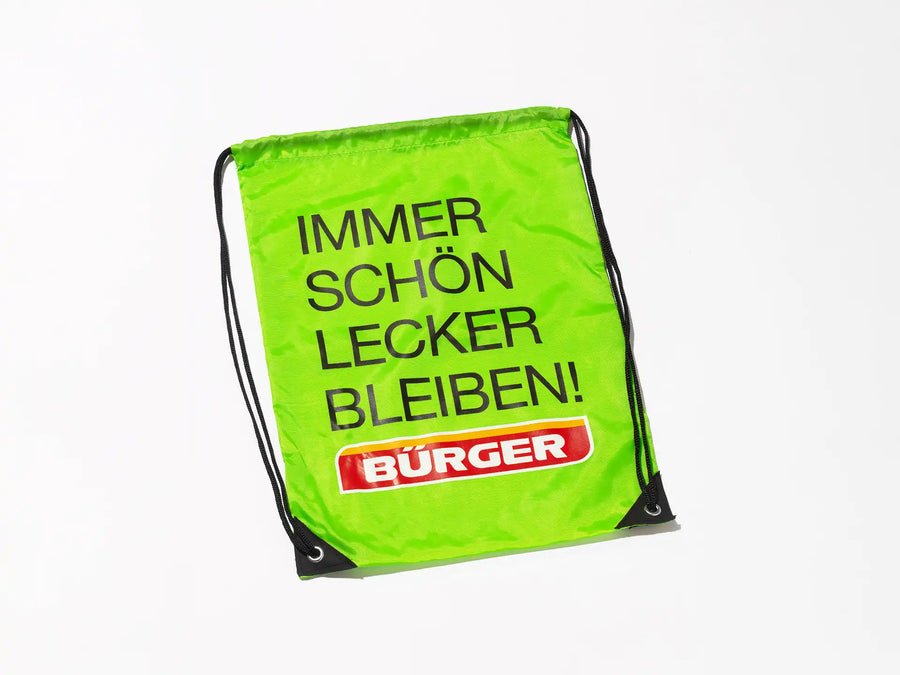 Grüner BÜRGER-Turnbeutel mit schwarzer Kordel und Aufdruck „IMMER SCHÖN LECKER BLEIBEN!“.