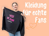 Frau hält Bürger Merchandise Pullover mit Aufdruck „YES! VE GAN! #teamburger“ vor orangem Hintergrund.