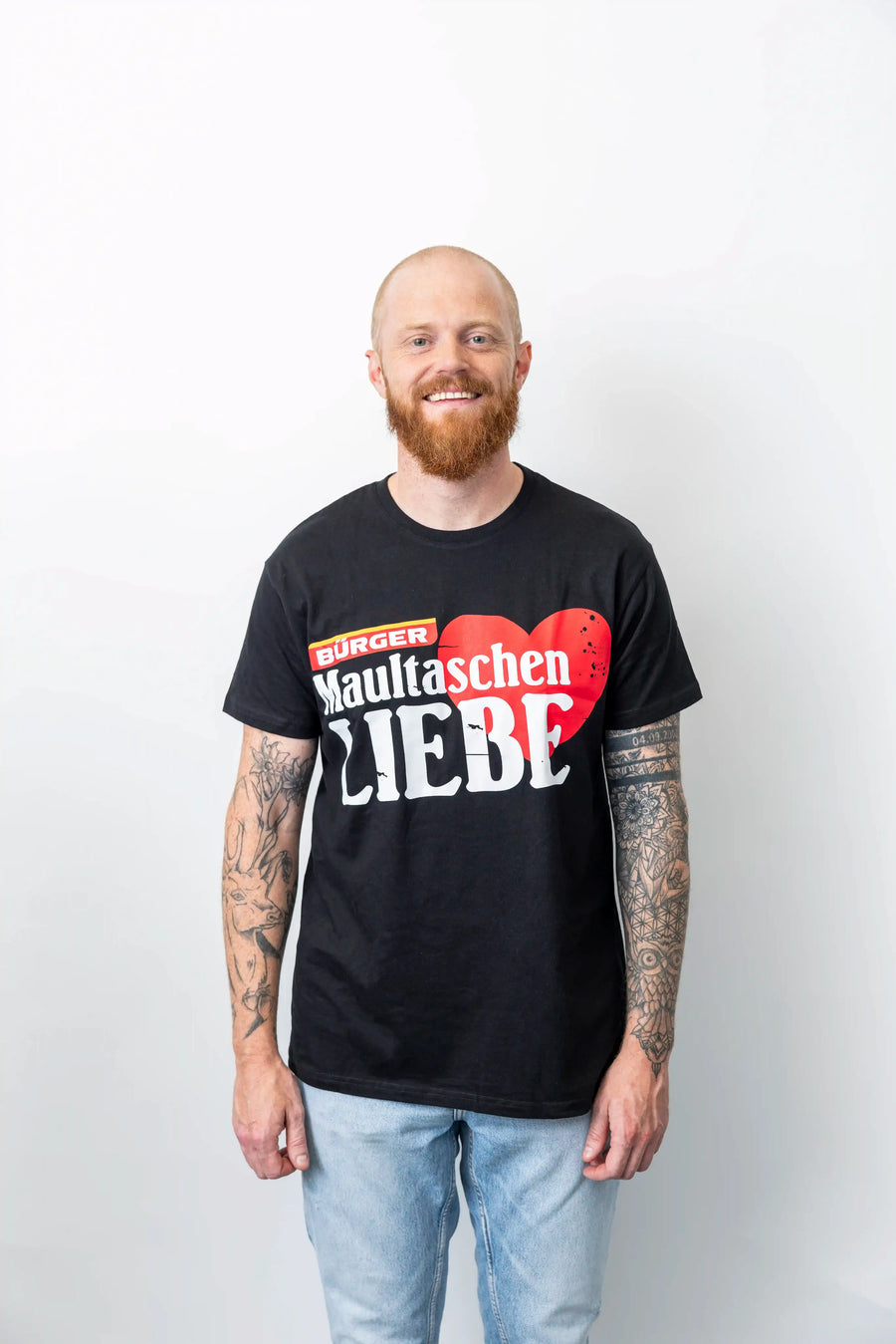 Mann steht vor weißem Hintergrund und trägt das schwarze BÜRGER-T-Shirt „Maultaschen Liebe“.