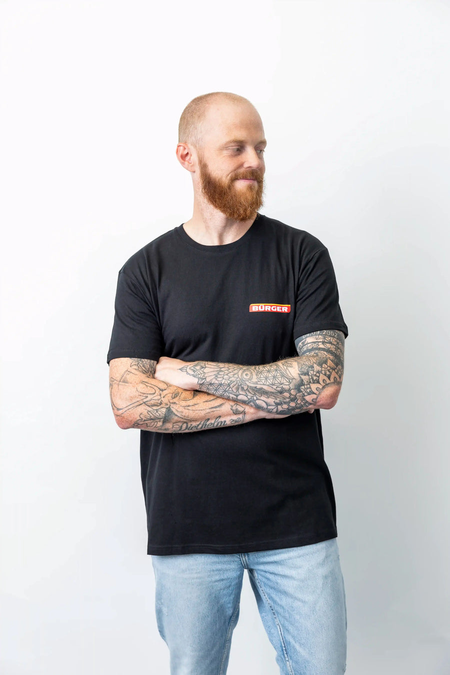 Mann mit tätowierten Armen trägt schwarzes BÜRGER-T-Shirt mit Logo auf der Brust.