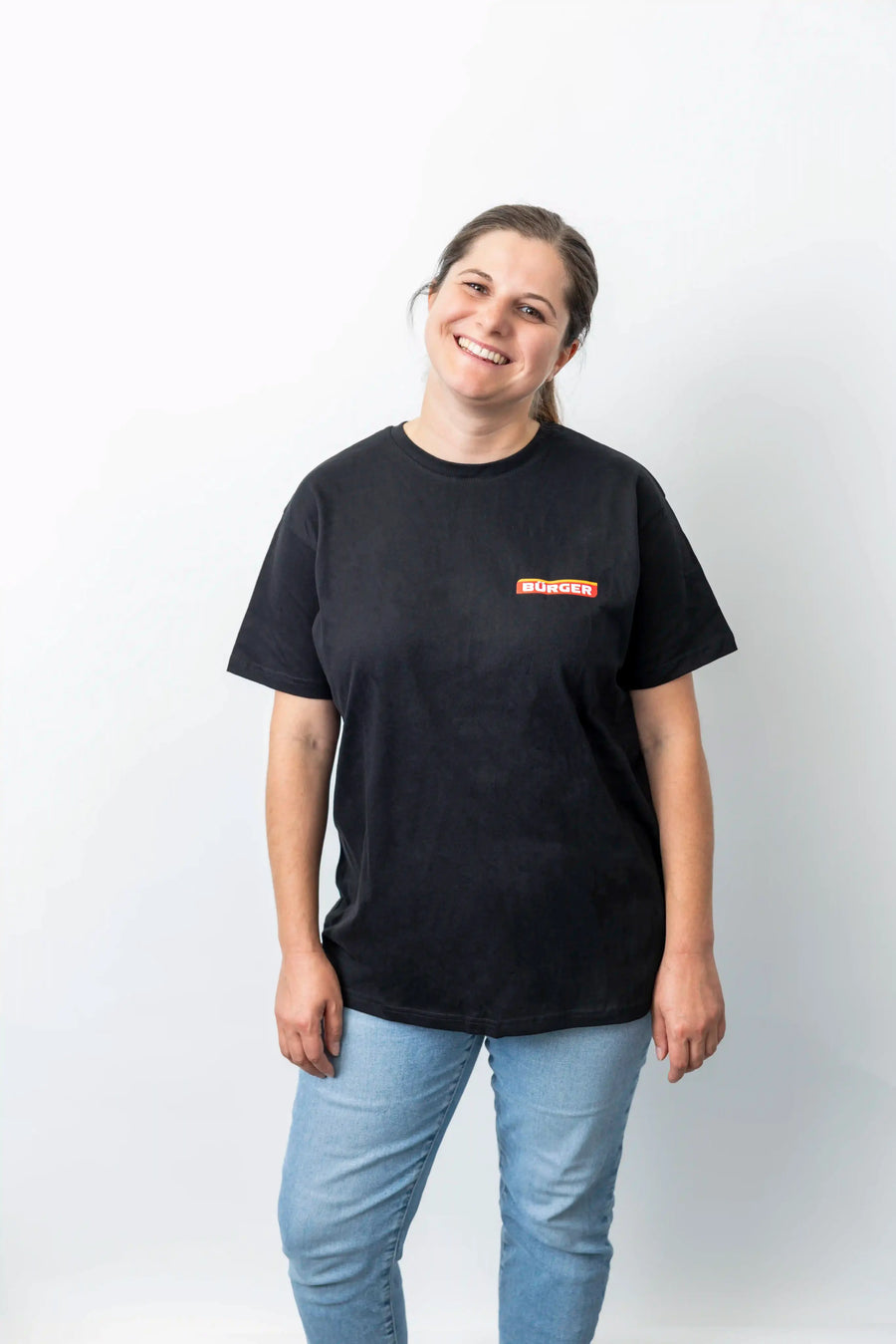 Frau mit BÜRGER-T-Shirt steht leicht schräg und lächelt vor hellem Hintergrund.