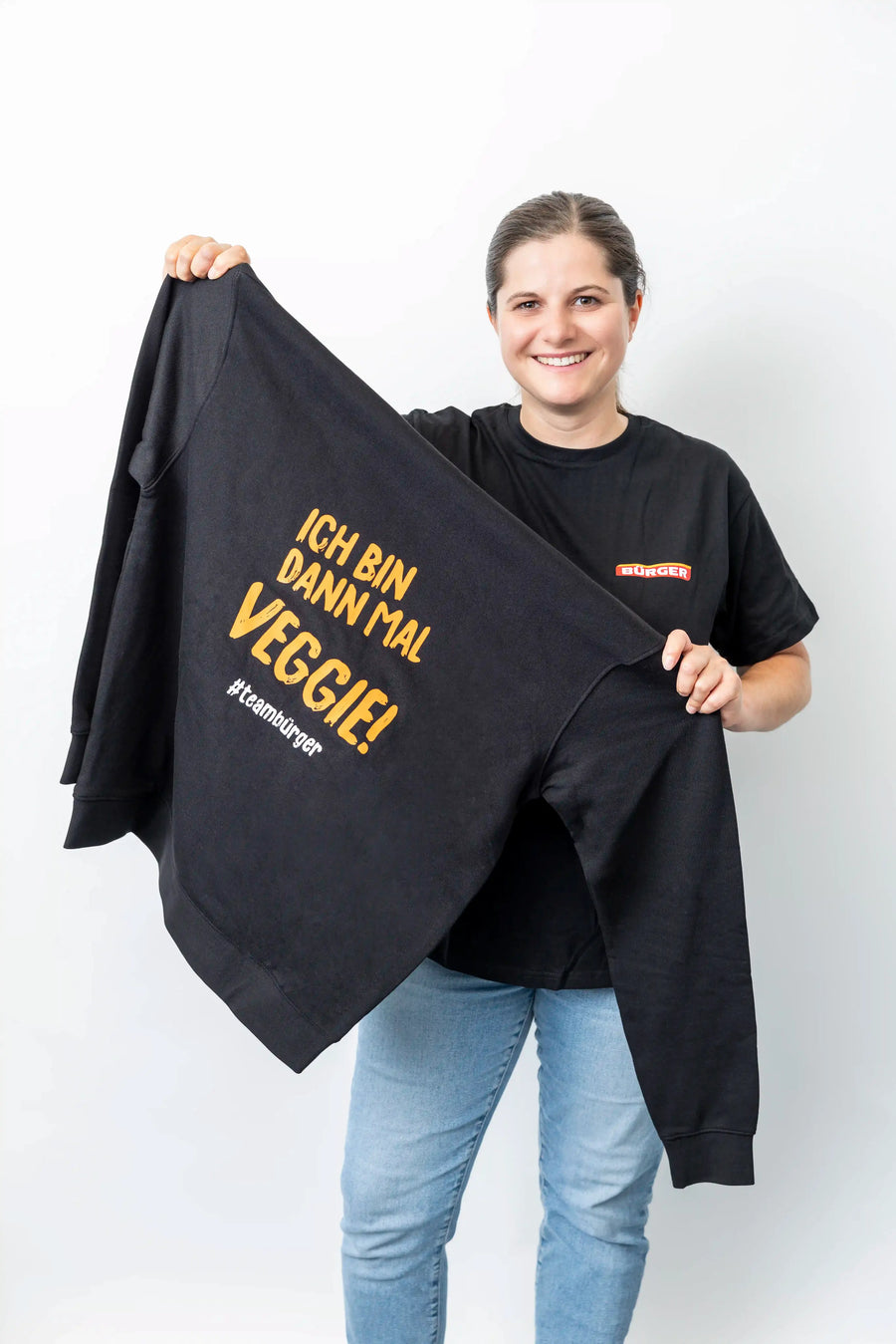 Frau zeigt schwarzen Sweater mit gelbem Aufdruck „Ich bin dann mal veggie! #teambürger“.