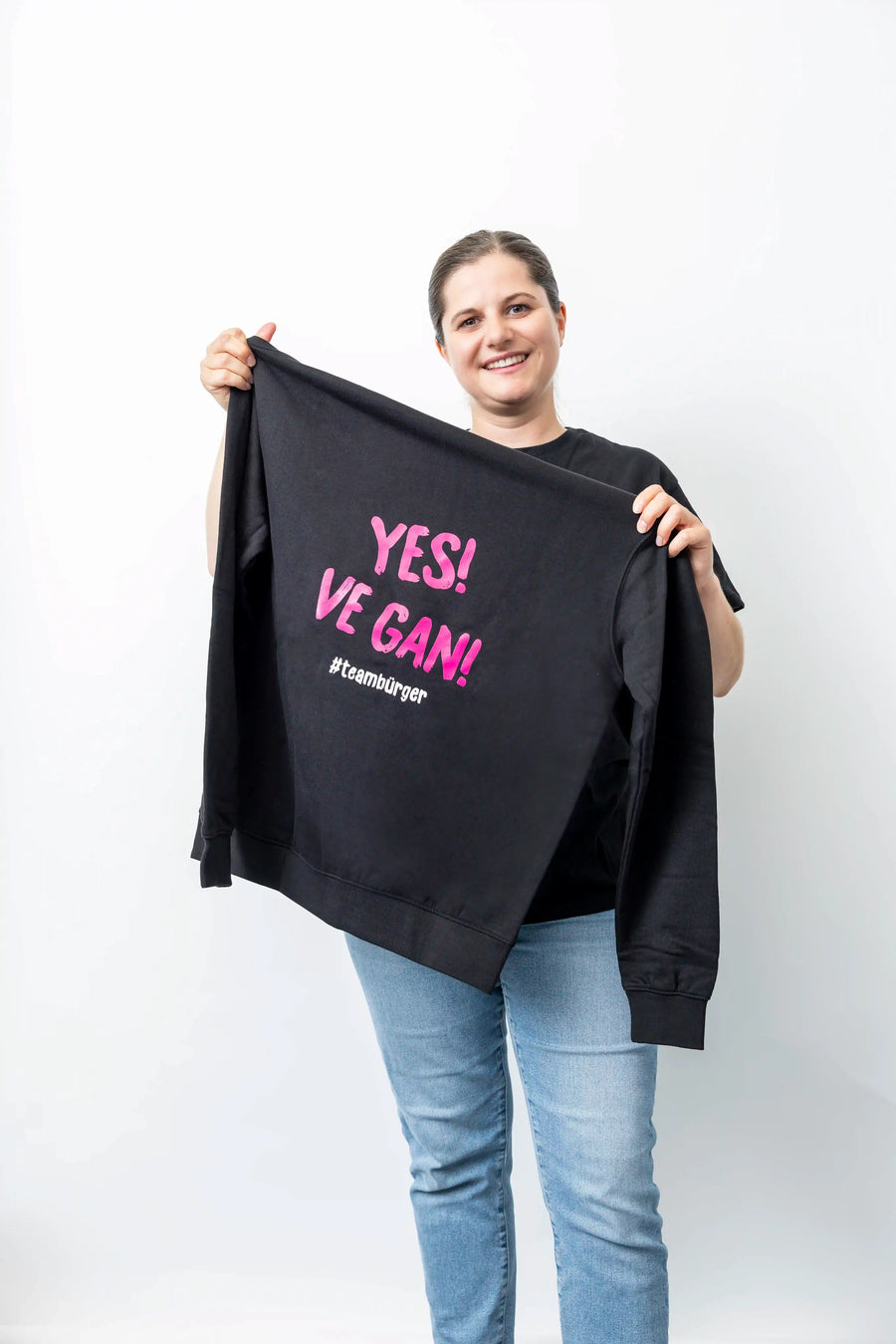Frau hält schwarzen Sweater mit pinkem Aufdruck „YES! VE GAN!“ und Hashtag #teambürger.