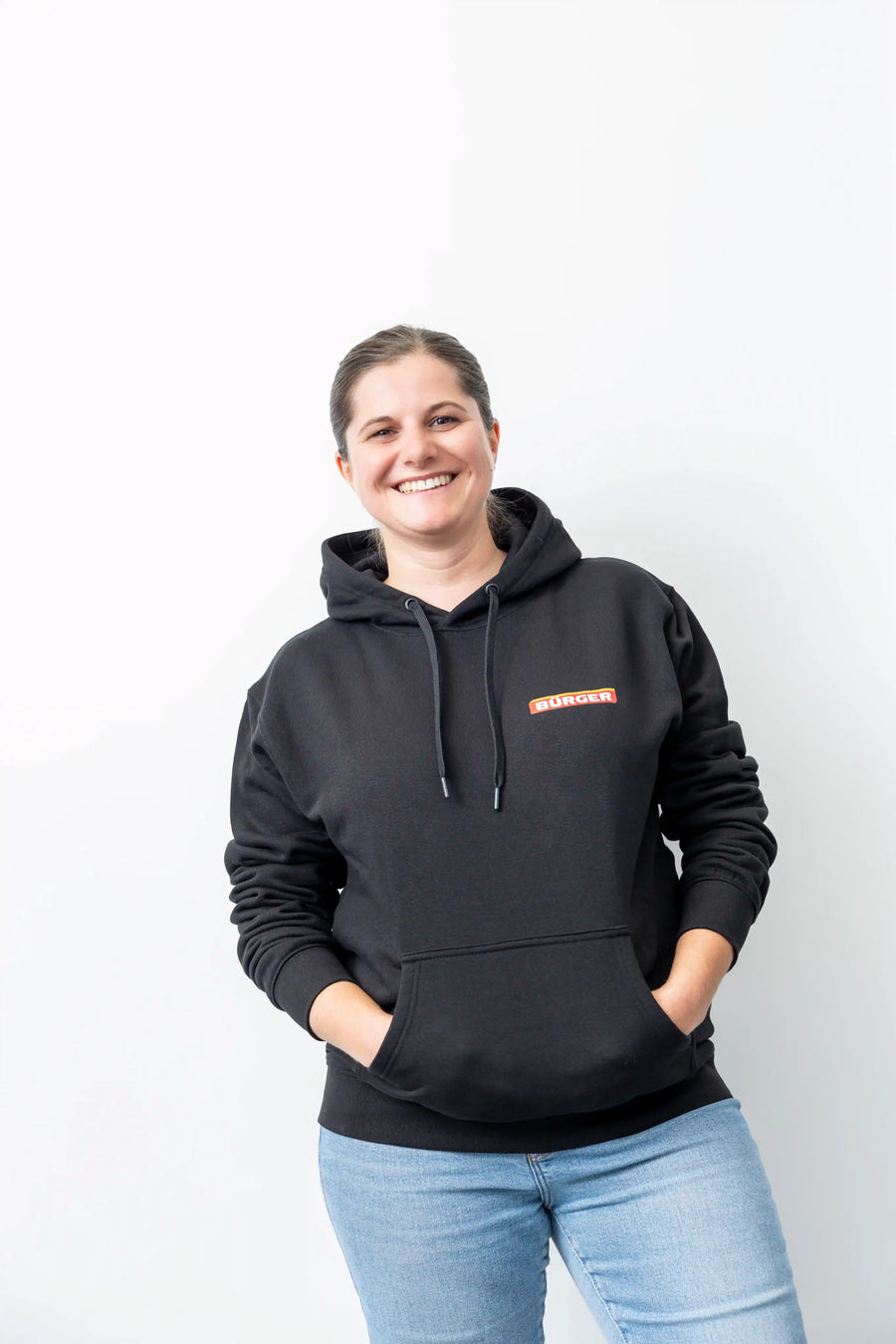 Frau mit schwarzem BÜRGER-Hoodie, beide Hände in der Kängurutasche, lächelt in die Kamera.