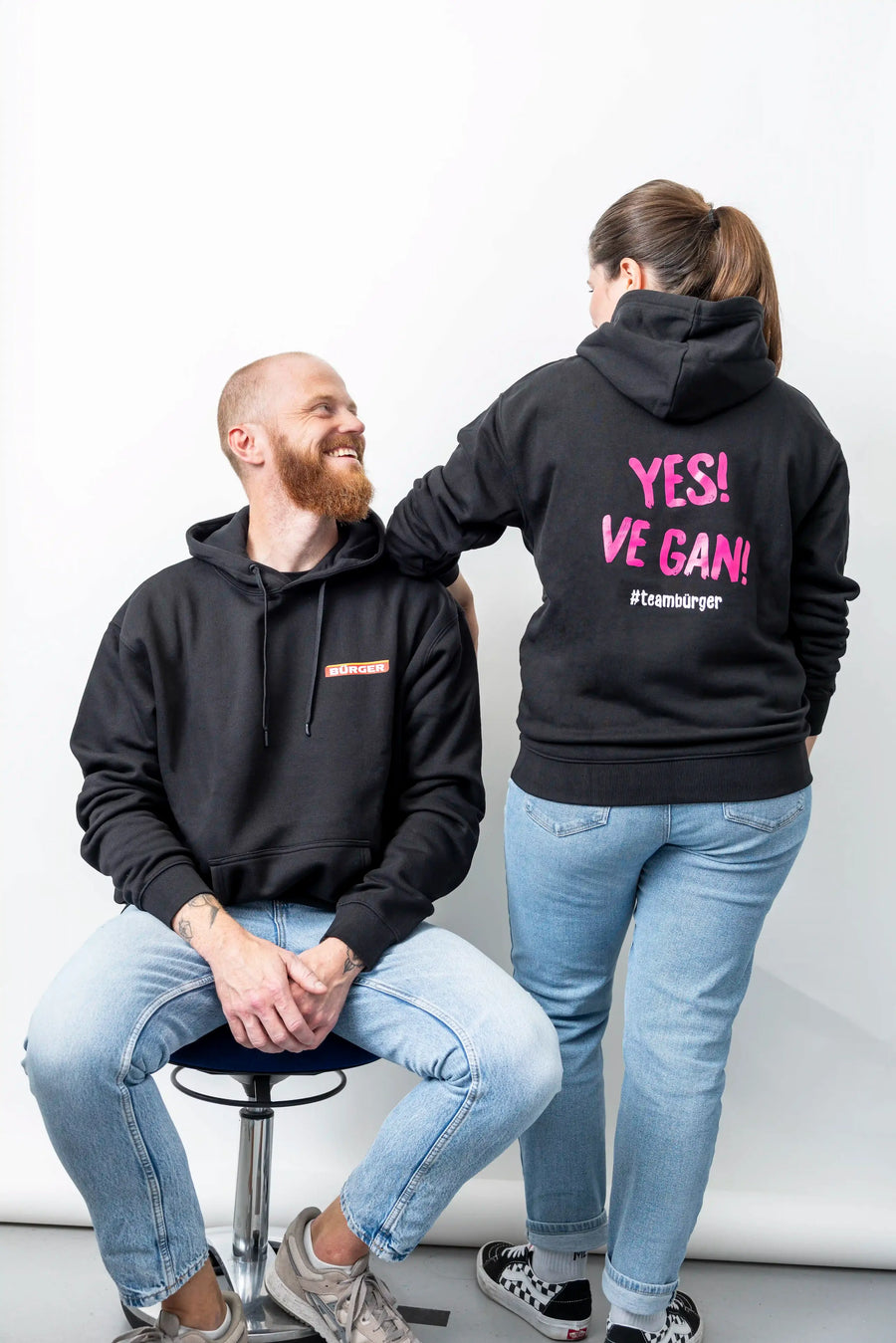 Frau zeigt Hoodie mit pinkem Aufdruck „YES! VE GAN!“, Mann trägt schwarzen BÜRGER-Hoodie.