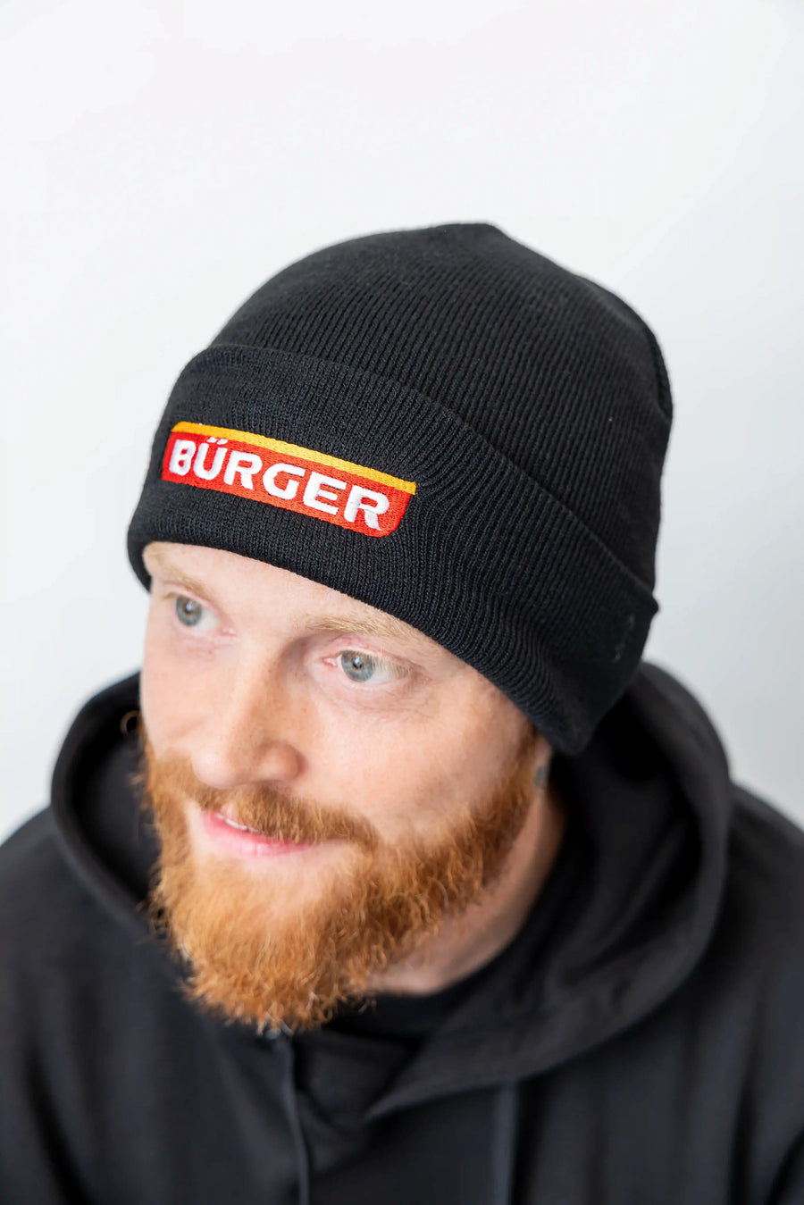 Nahaufnahme eines Mannes mit schwarzer BÜRGER-Beanie und schwarzem Hoodie.