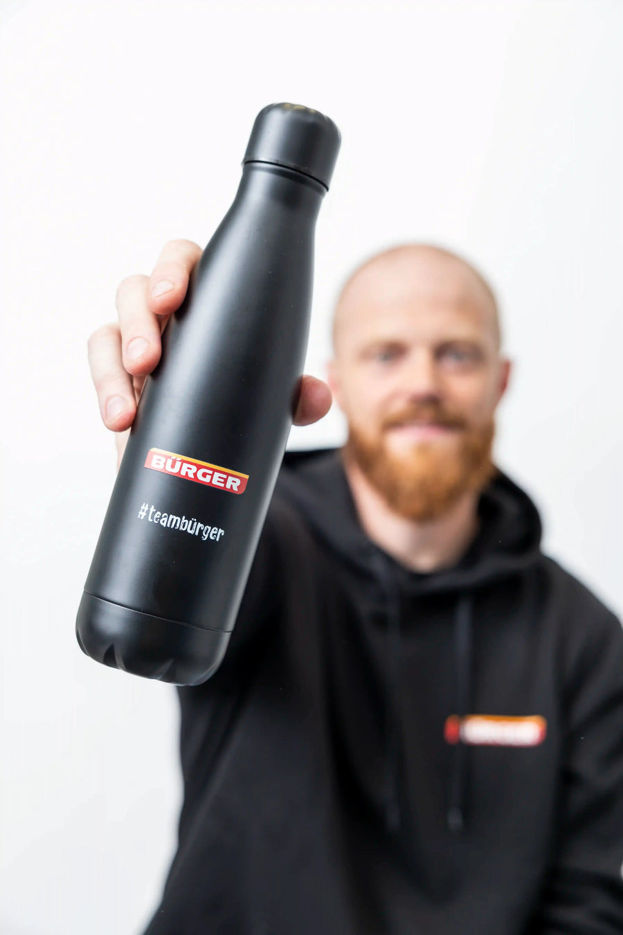 Mann hält schwarze BÜRGER-Trinkflasche mit Aufdruck „#teambürger“ in die Kamera.